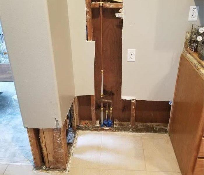 Photo is showing drywall removed from walls around and behind where the refrigerator was due to water damage