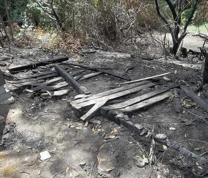 Photo is showing a burned and charred wooden fence on the ground.