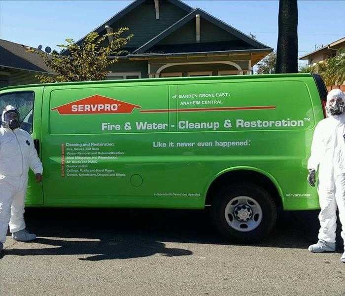Photo is showing 2 technicians standing next to their SERVPRO green vehicle, wearing full PPE gear 
