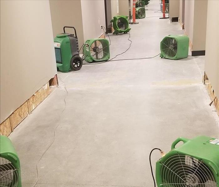 Photo is showing a long hallway in a commercial building with air movers (fans) placed all along the walls drying them.