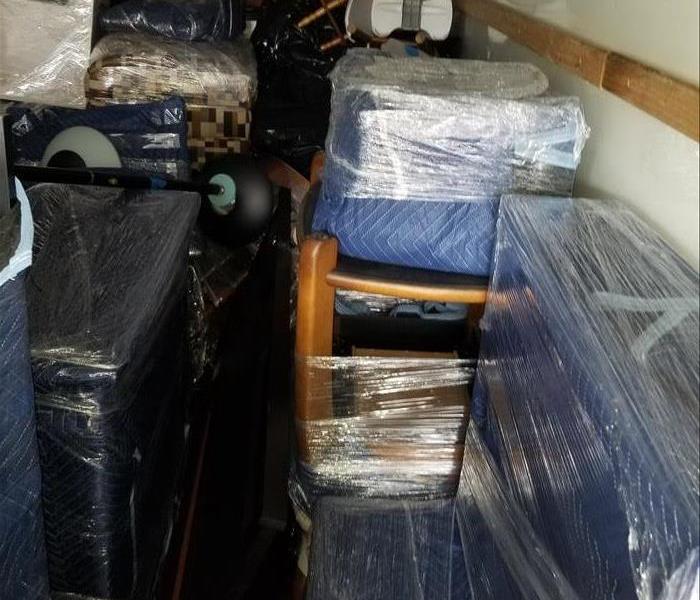 Photo is showing furniture wrapped in blankets and plastic and stored in a storage facility