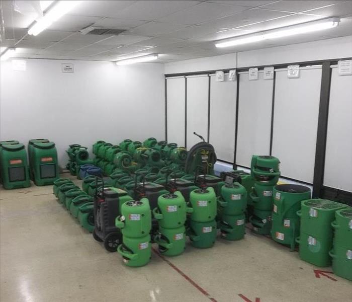 Photos is showing neatly stacked SERVPRO green air movers and dehumidifiers ready to be placed inside a commercial building