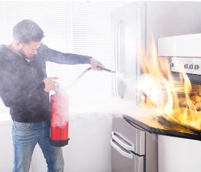 Man standing in the kitchen, holding fire extinguisher, putting out a stovetop fire 
