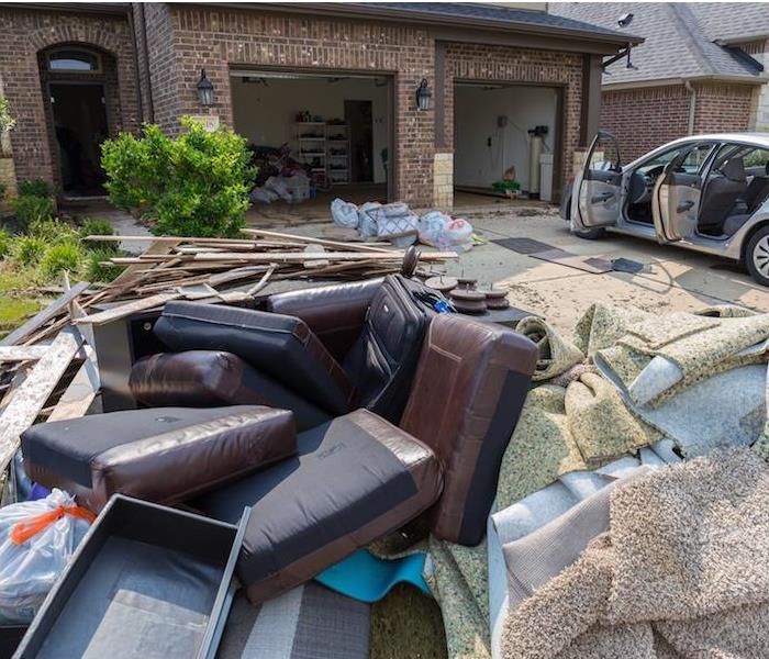 Photo shows unsalvageable contents in the driveway of a home due to water damage in the home and garage. 