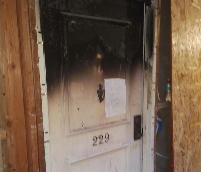 An Apartment door after a fire showing the door and frame charred by flames from the fire.