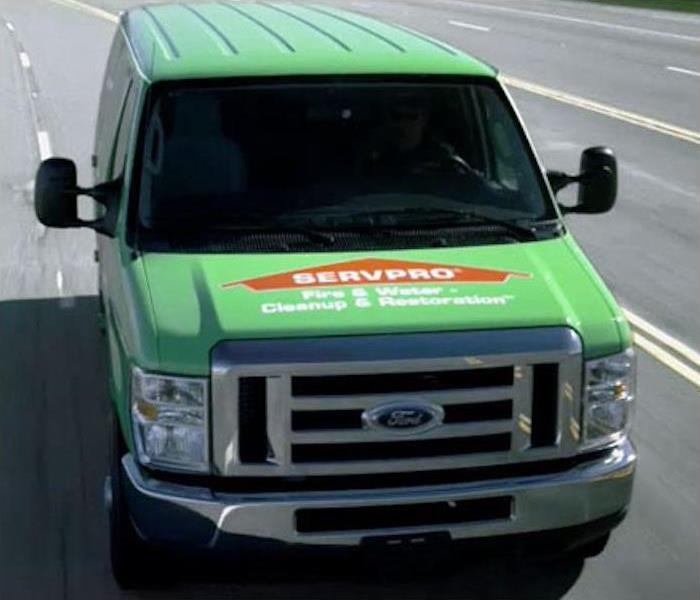 Photo is showing a green SERVPRO Van driving on the road with the SERVPRO House logo on the front of the hood. 