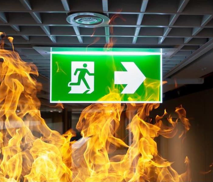 Photo is showing a fire in a commercial building with a green exit sign with an arrow showing which direction the exit is.