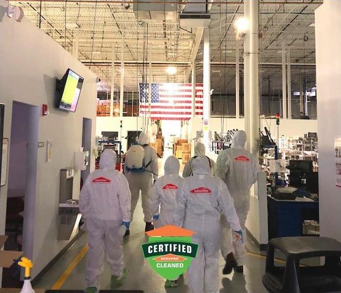 Photo is showing SERVPRO Technicians wearing PPE gear. They're walking into a jobsite with an American Flag in front of them.